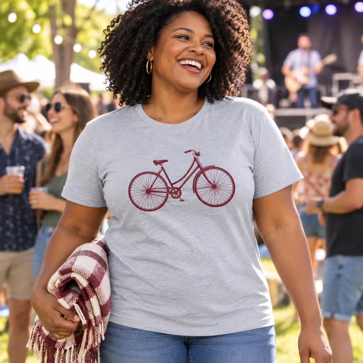 Model wearing a heather gray Bella + Canvas Ultra-Soft Jersey unisex T-shirt with fictional bicycle sample artwork at a music festival.