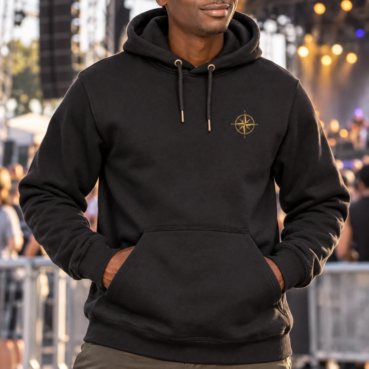 Close view of a man wearing a black hoodie with fictional gold compass sample artwork at an outdoor music venue.