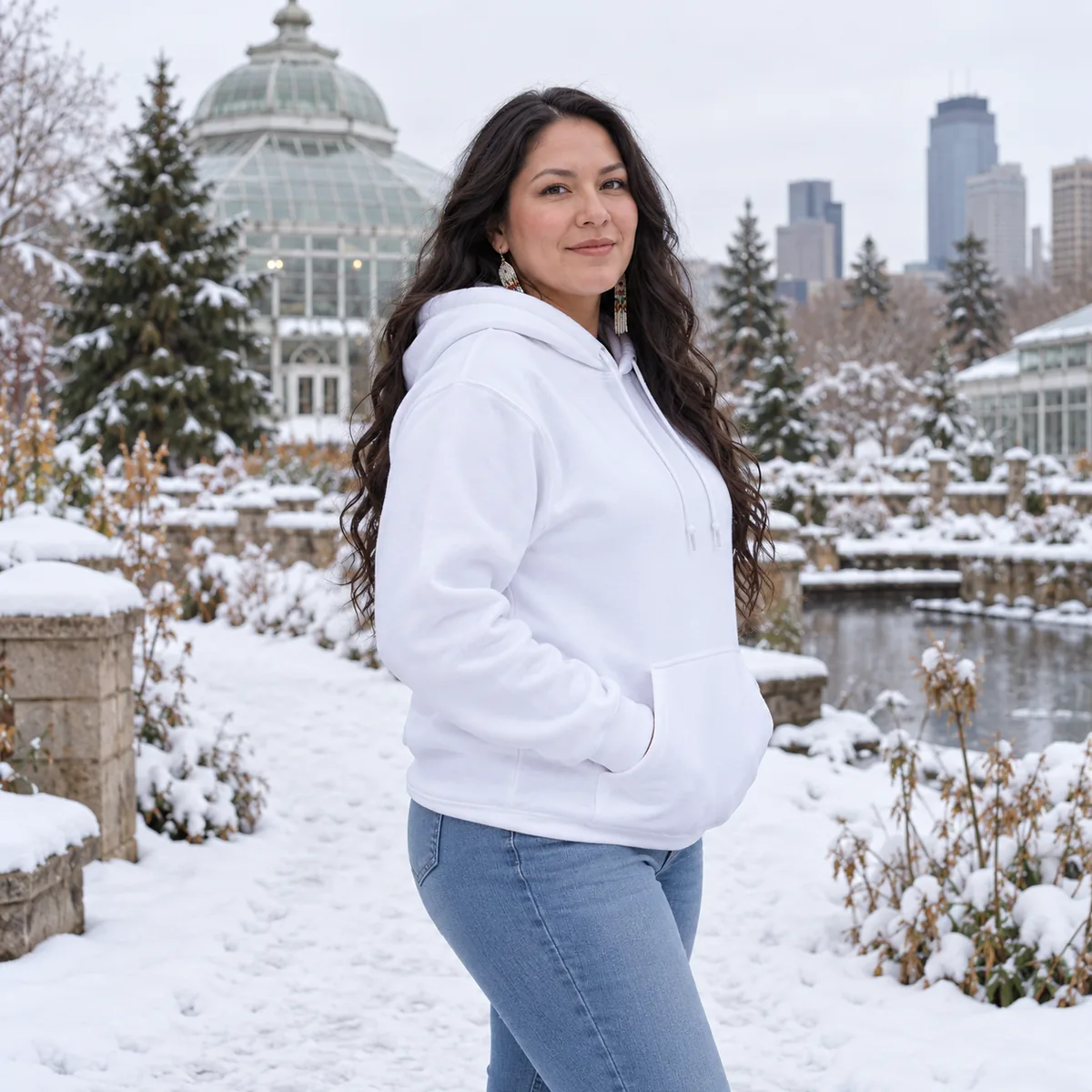Indigenous woman wearing a white Champion Powerblend hoodie at a snowy urban botanical garden.