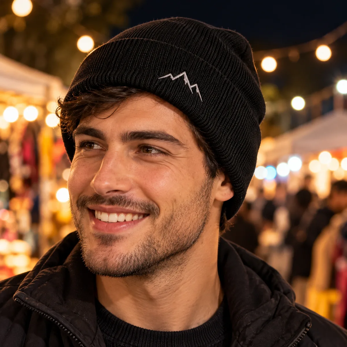 Close view of a man wearing a black cuffed beanie with fictional silver mountain embroidery at a night market.