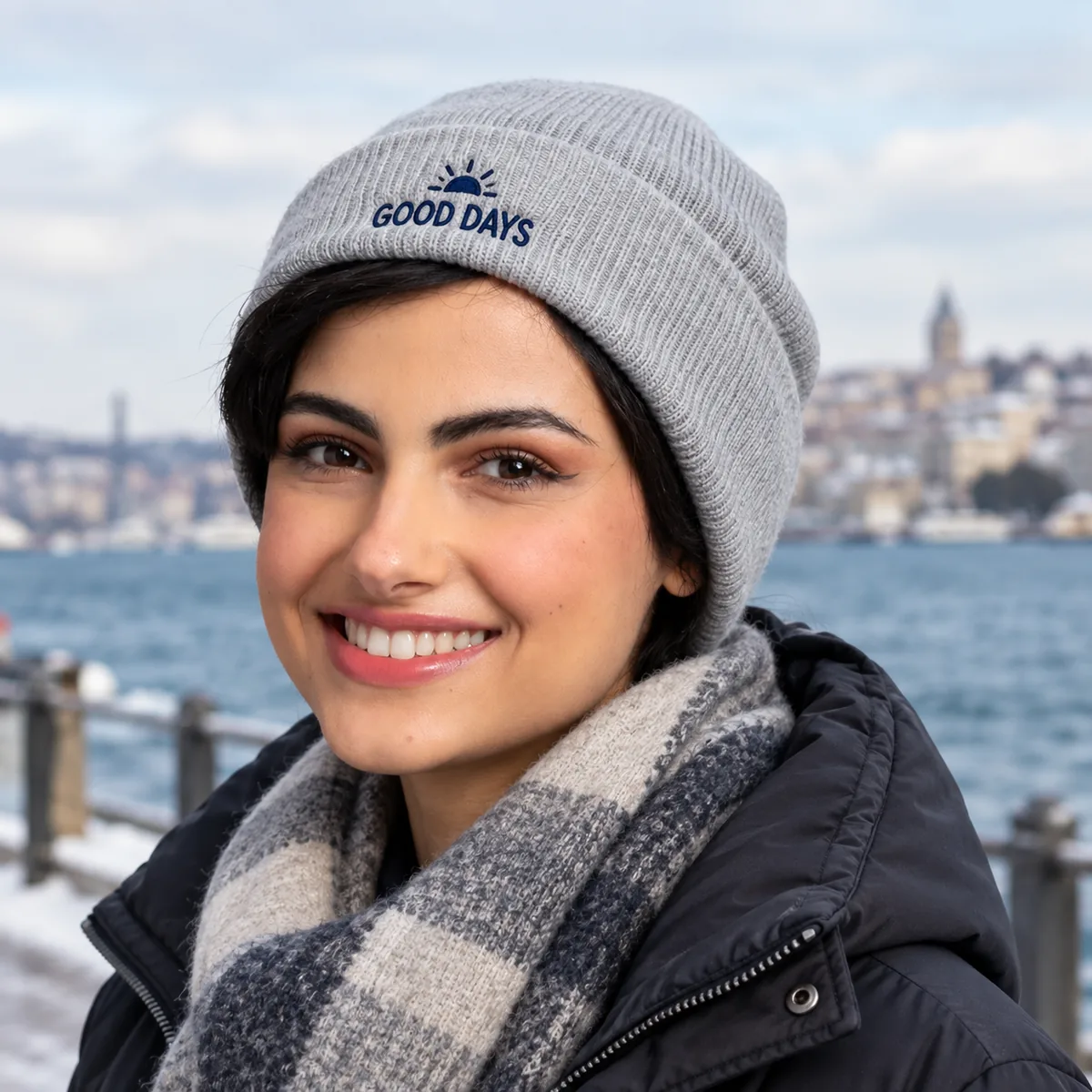 Woman wearing a light grey beanie with fictional Good Days sample embroidery at a waterfront.