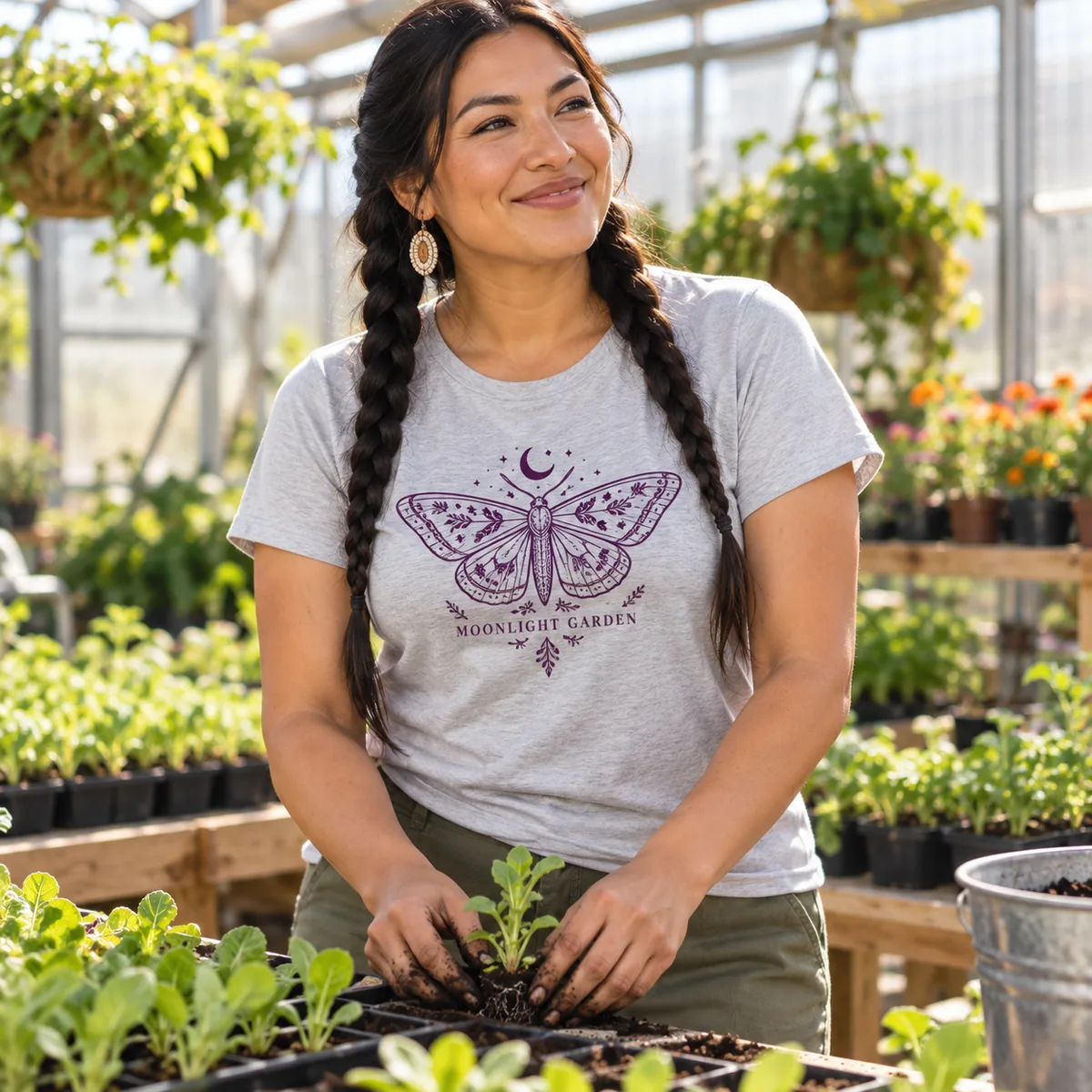 Woman wearing a light heather gray District Soft-Touch Women’s T-shirt with fictional Moonlight Garden sample artwork in a greenhouse.