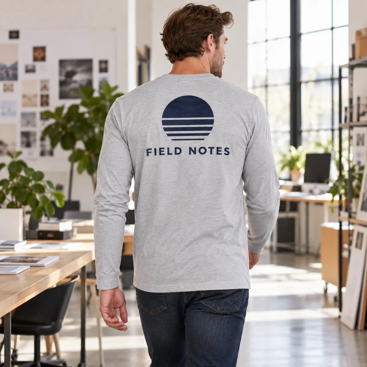 Man wearing the light heather grey long-sleeve tee with fictional Field Notes sample back artwork at a design studio.