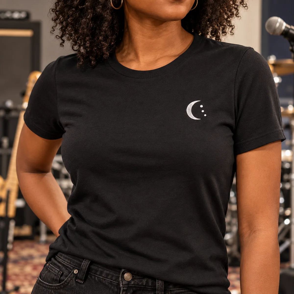 Close view of a woman wearing the black tee with a small fictional crescent sample mark at a music rehearsal room.