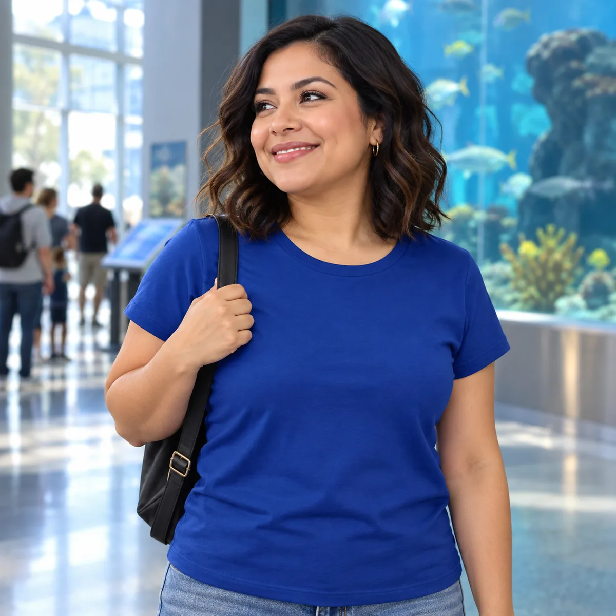 Woman wearing the deep royal District Women’s Very Important Tee in an aquarium lobby; blank front view.