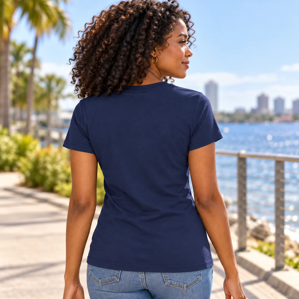 Woman wearing the new navy District Women’s Very Important Tee, shown from behind on a waterfront path; blank back.