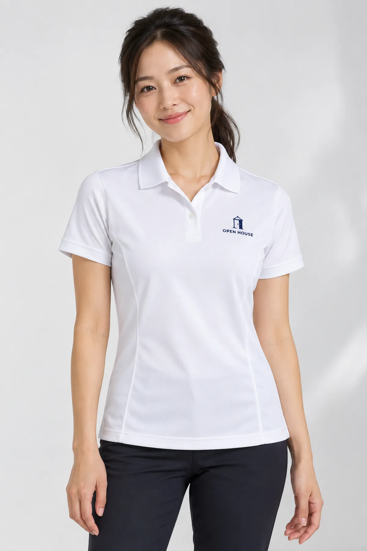 Woman wearing a white solid Elevate Moreno polo with fictional Open House sample branding in a bright studio.