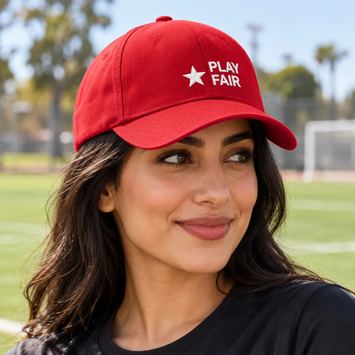 Woman wearing a red cap with fictional Play Fair embroidered branding at a community sports field.