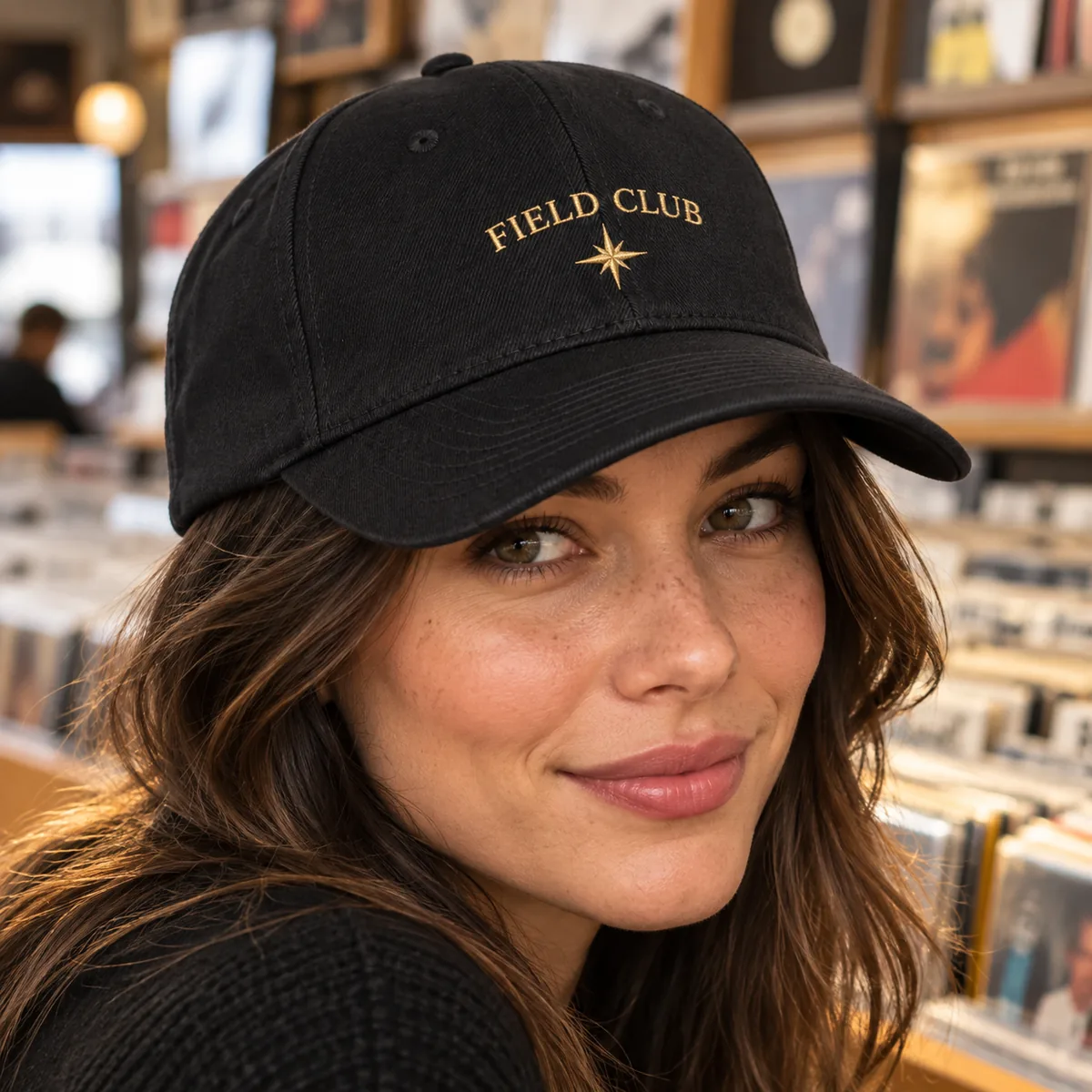 Close view of a woman wearing a black fitted cap with fictional Field Club gold sample embroidery at a record shop.