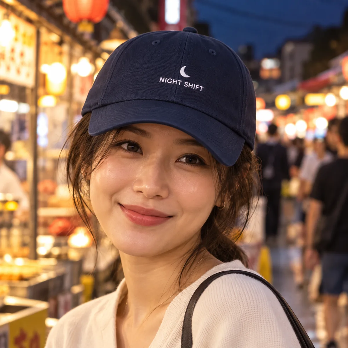 Woman wearing a dark navy fitted cap with fictional Night Shift sample branding at an evening market.