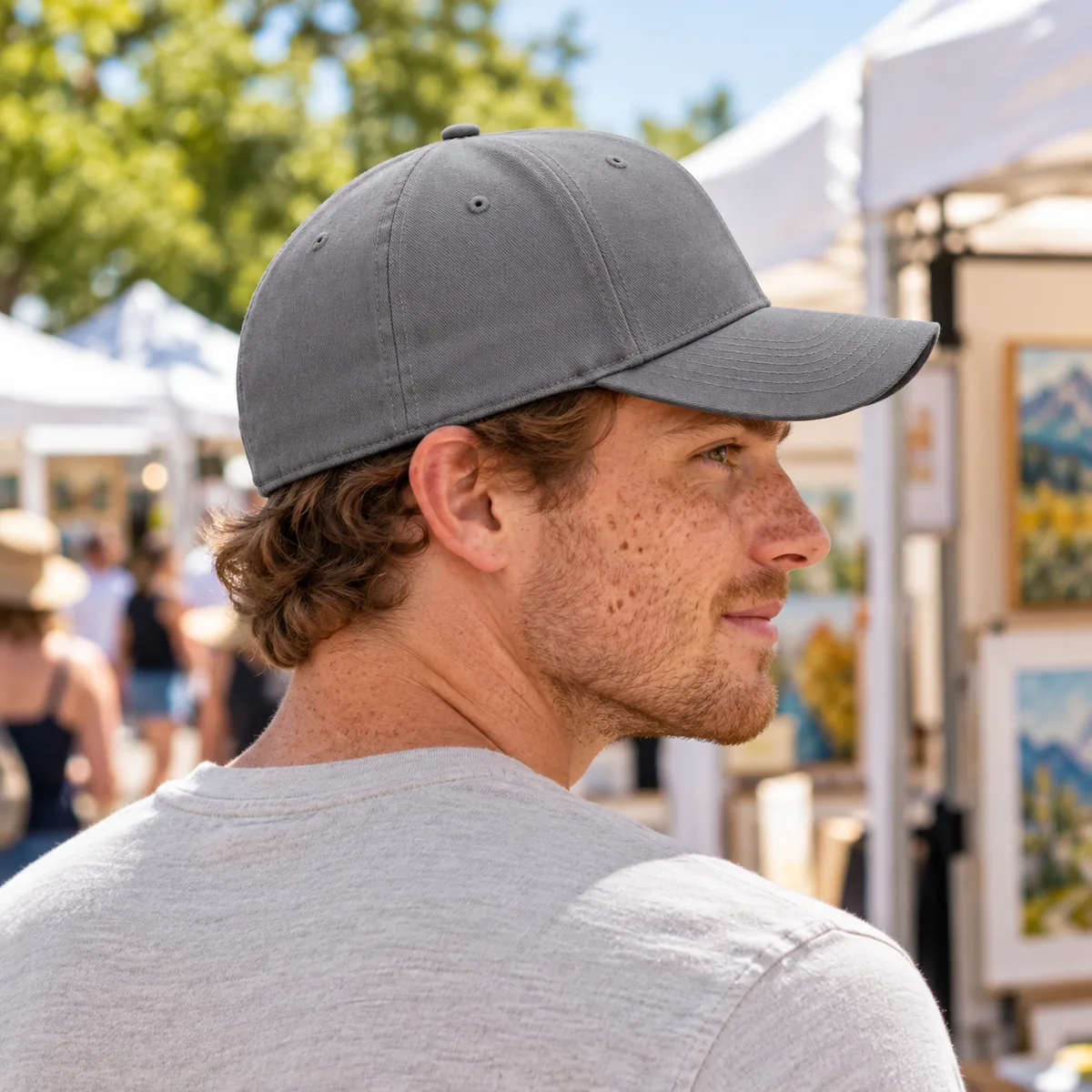 Man wearing a medium grey fitted Flexfit cap, shown from behind at an outdoor art fair.