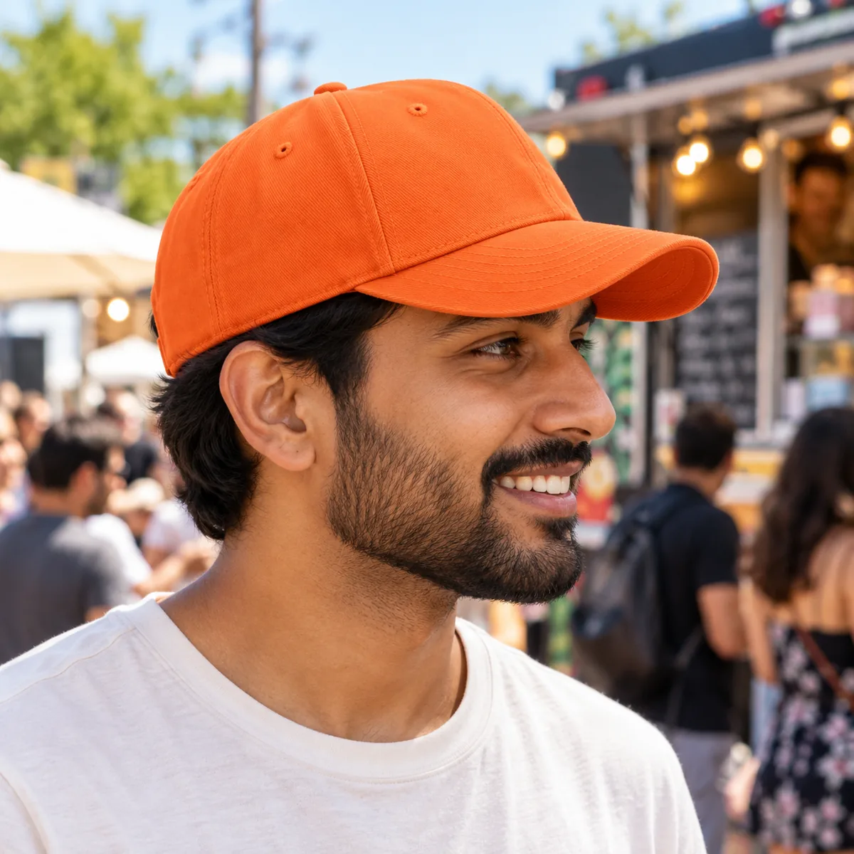 Man wearing an orange blank Flexfit cap in side profile at a food truck festival.