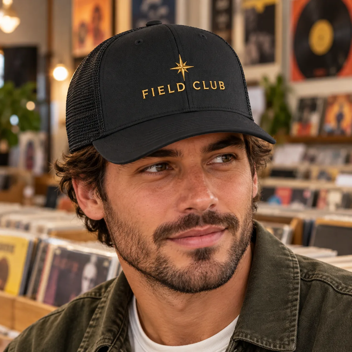 Close view of a man wearing a black trucker cap with fictional Field Club sample embroidery at a record shop.