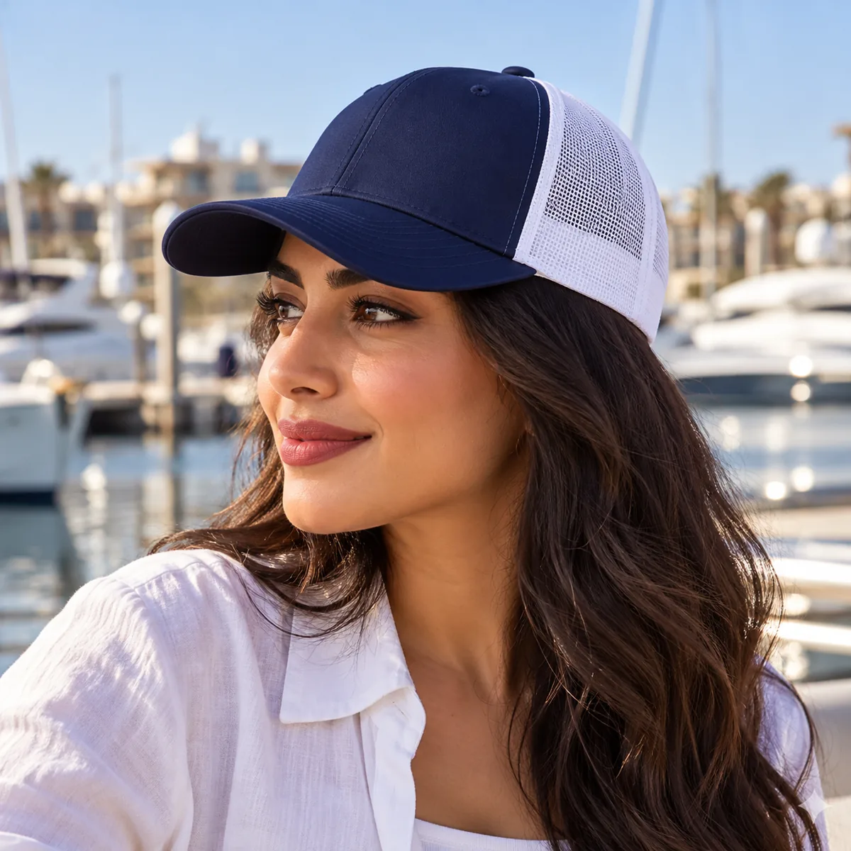 Woman wearing a navy and white trucker cap at a marina, shown in side view.