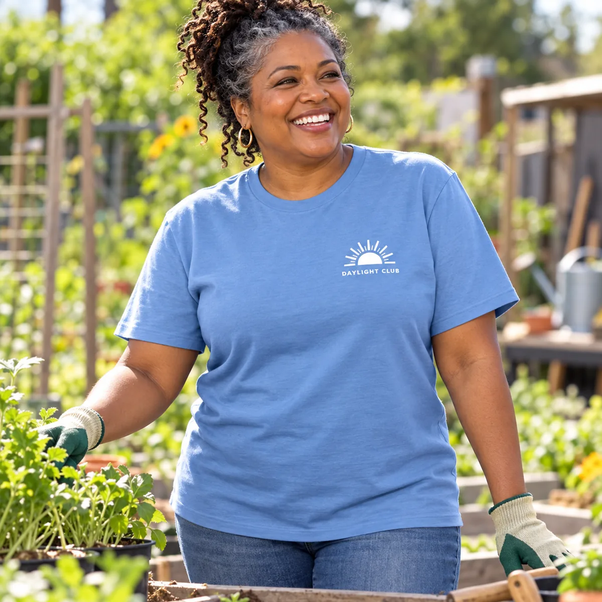 Model wearing a light blue Gildan Budget unisex T-shirt with fictional Daylight Club sample branding in a community garden.