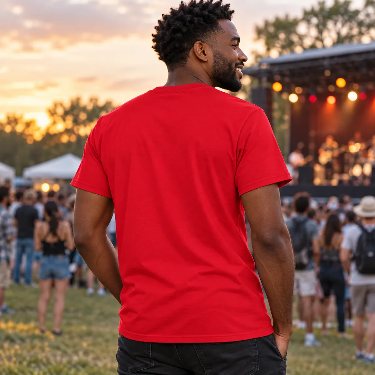 Man wearing a red Gildan DryBlend T-shirt at a community music event, shown from the back.