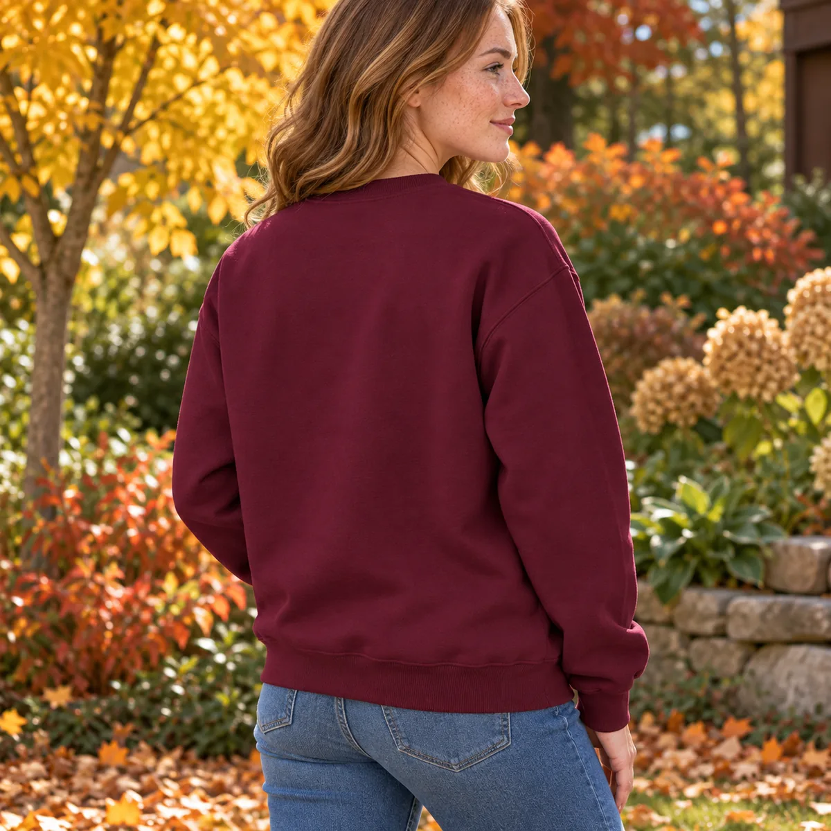 Woman wearing a maroon Gildan Heavy Blend sweatshirt in an autumn garden, shown from behind.