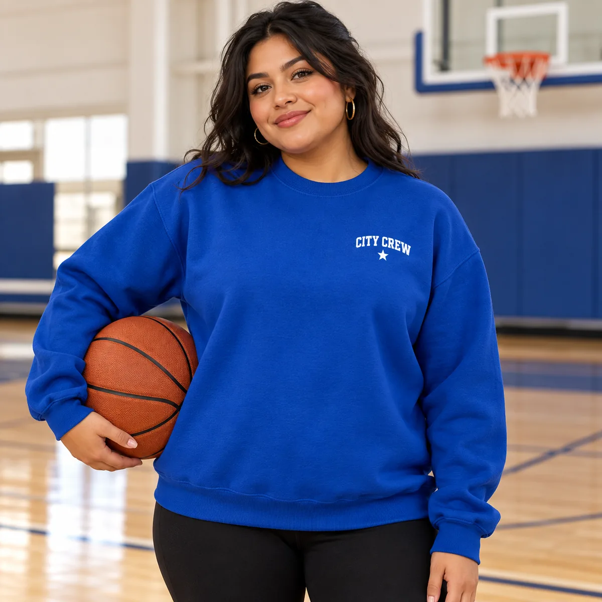 Woman wearing a royal blue Gildan Heavy Blend sweatshirt with fictional City Crew sample branding at a basketball court.