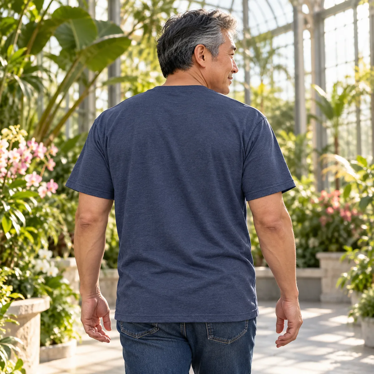 Back view of a model wearing a heather navy Gildan Ultra Cotton unisex T-shirt in a botanical conservatory.