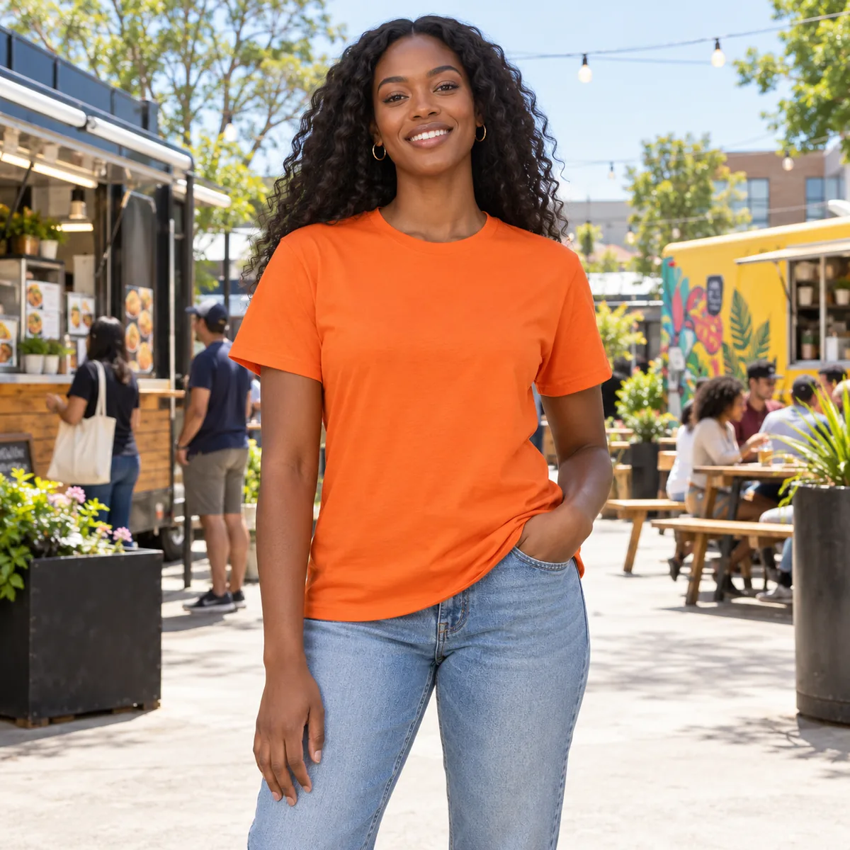 Black woman wearing an orange Hanes Essential T-shirt at a neighborhood food truck courtyard.