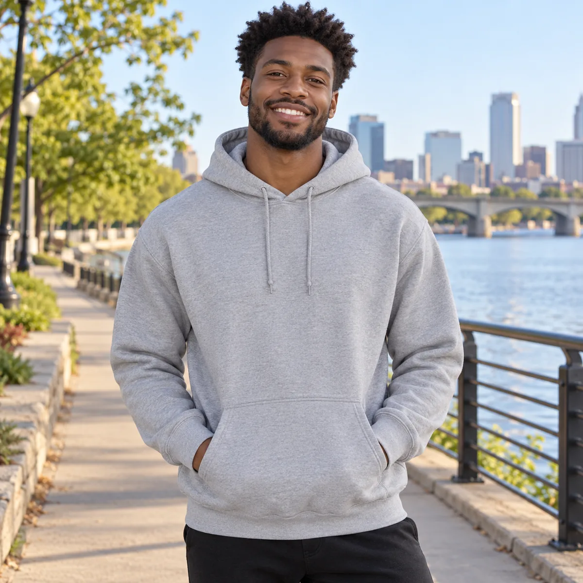 Black man wearing an Oxford JERZEES NuBlend hooded sweatshirt on a city riverside path.