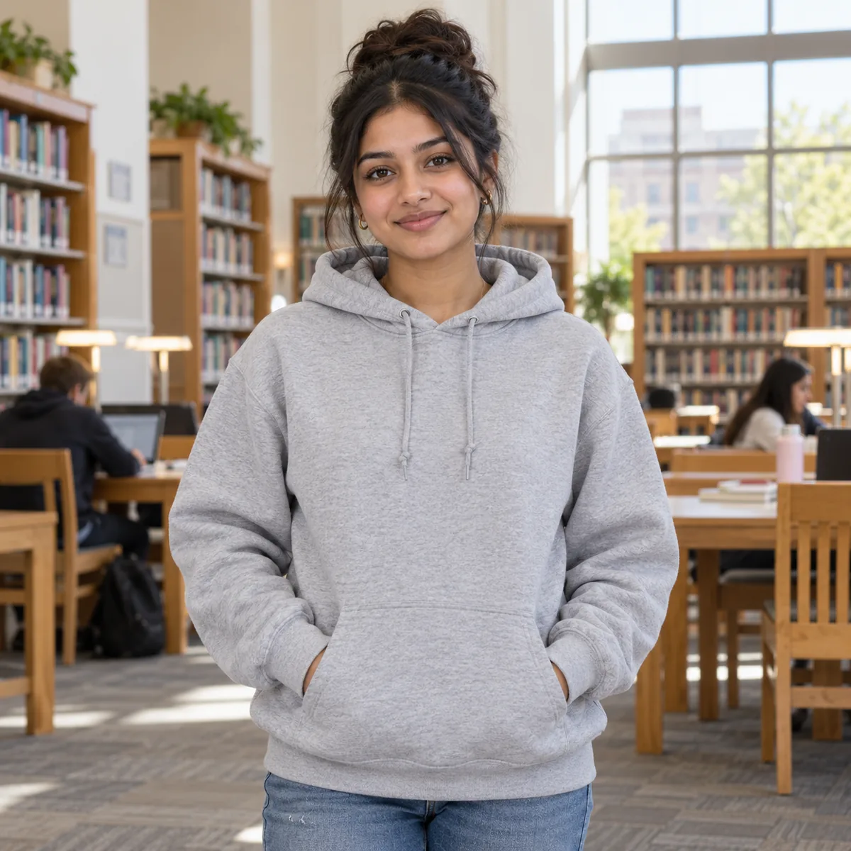 South Asian woman wearing an athletic heather JERZEES NuBlend hoodie in a university library.