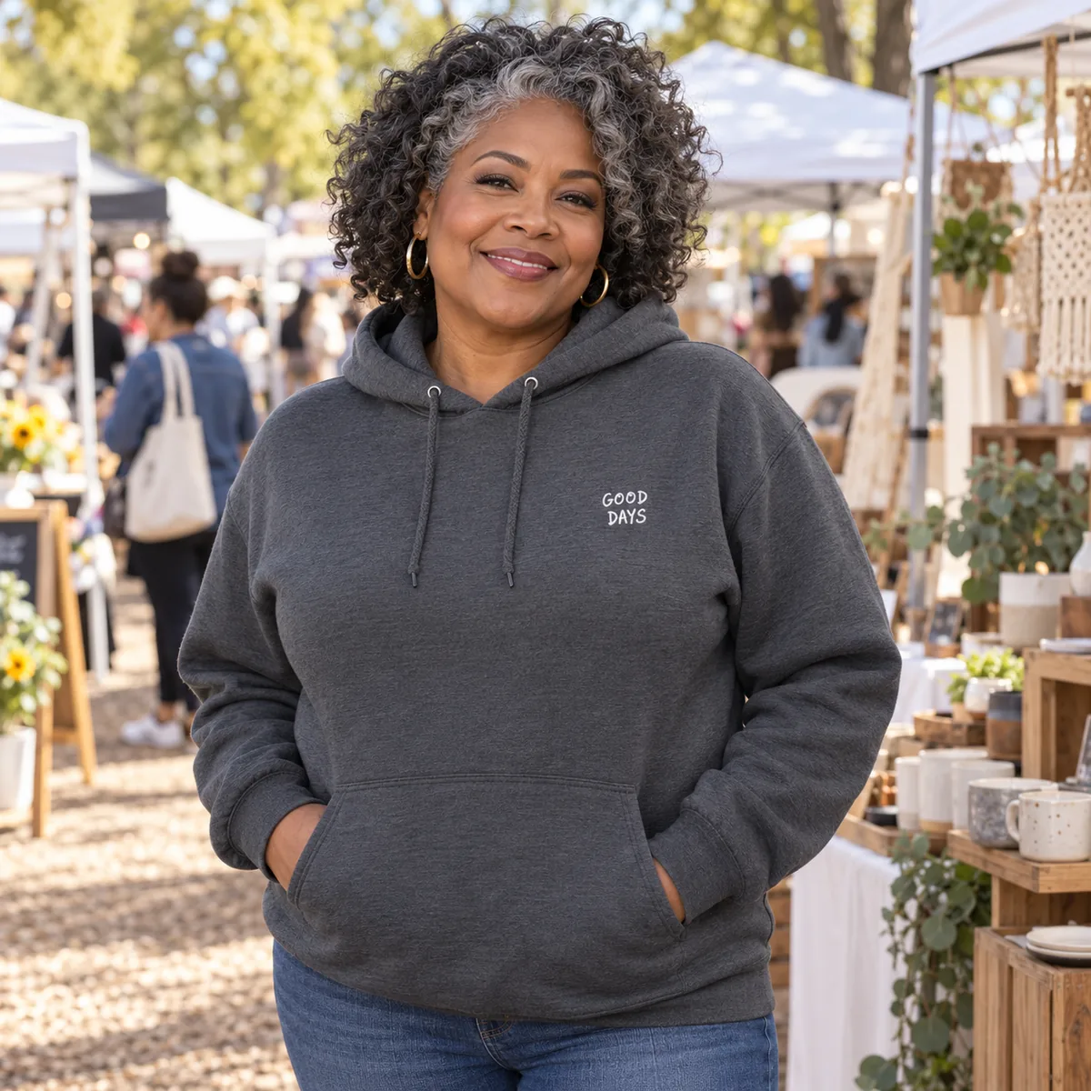 Black woman wearing a charcoal grey JERZEES NuBlend hoodie with fictional Good Days embroidery at an outdoor makers market.