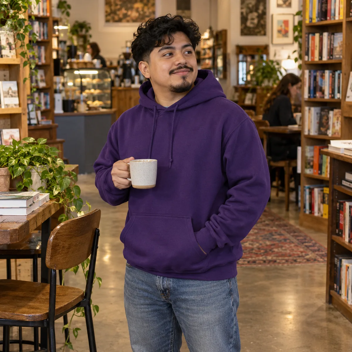 Latino man wearing a deep purple JERZEES NuBlend hoodie at a bookstore cafe.