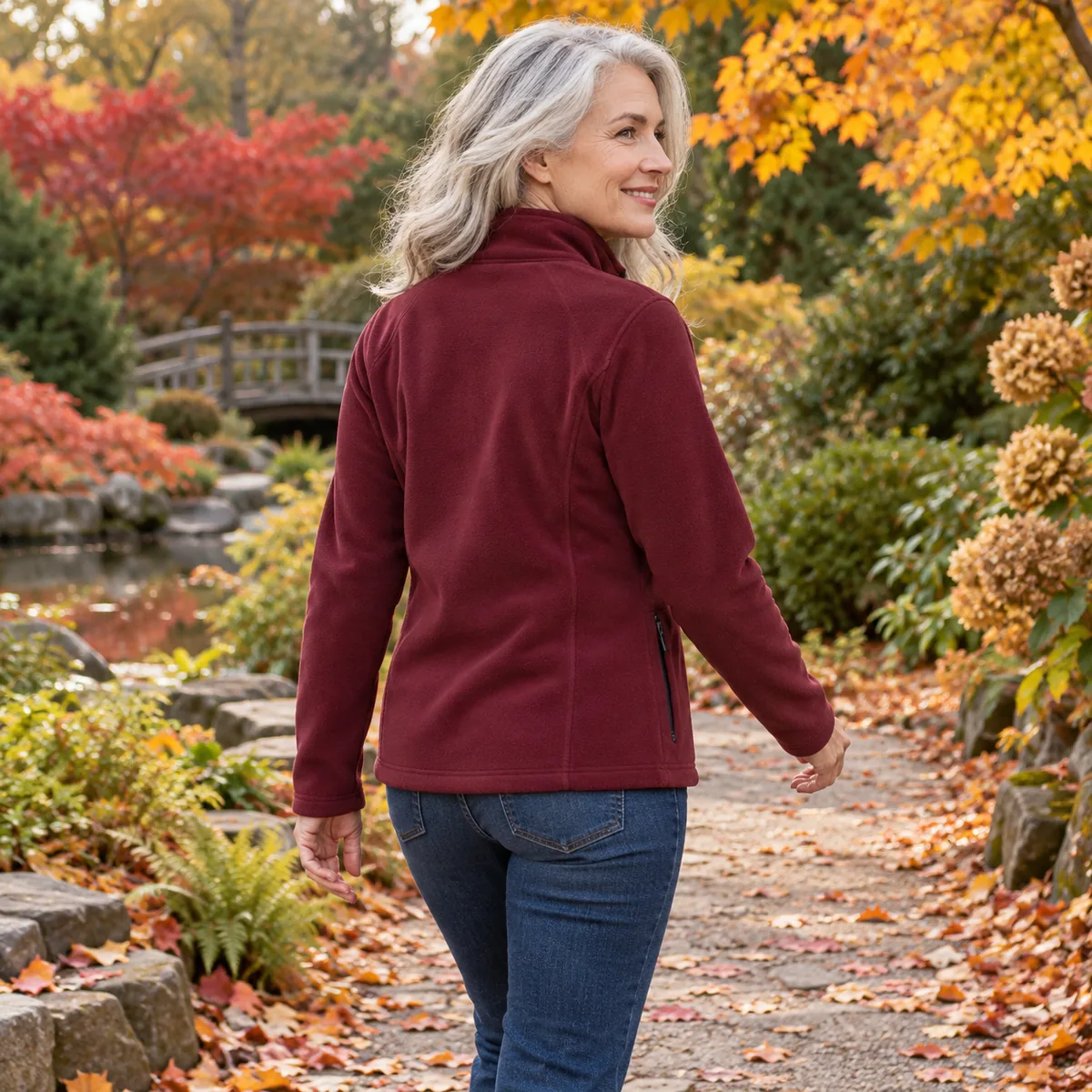 Silver-haired woman wearing a maroon women’s fleece jacket, shown from behind in an autumn garden.