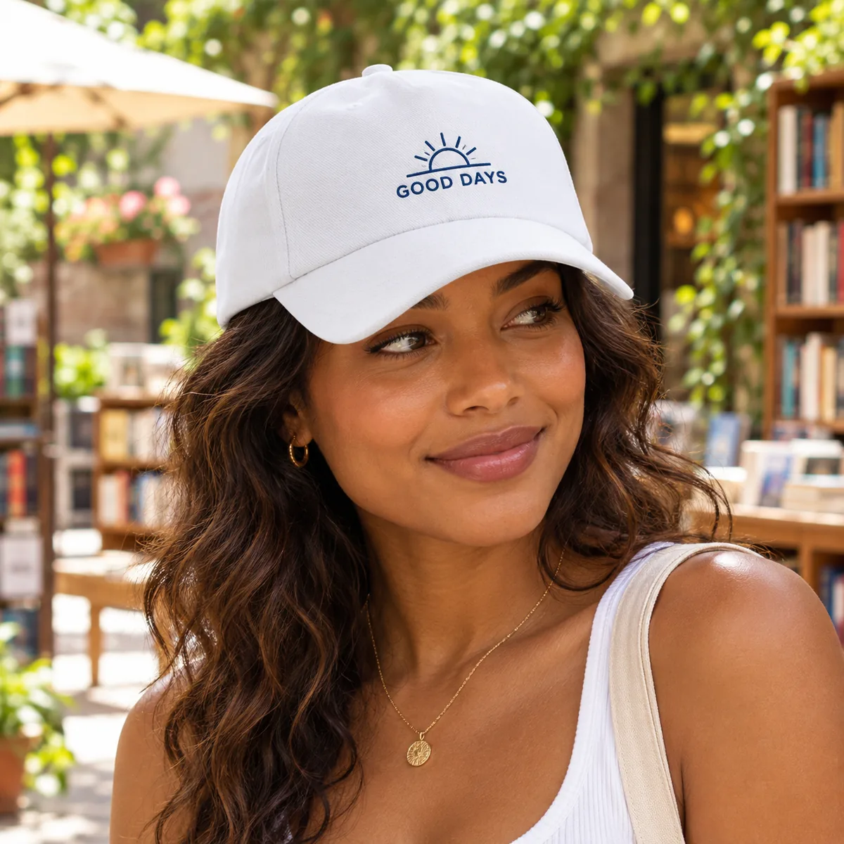 Woman wearing a white baseball cap with fictional Good Days sample branding in a bookstore courtyard.