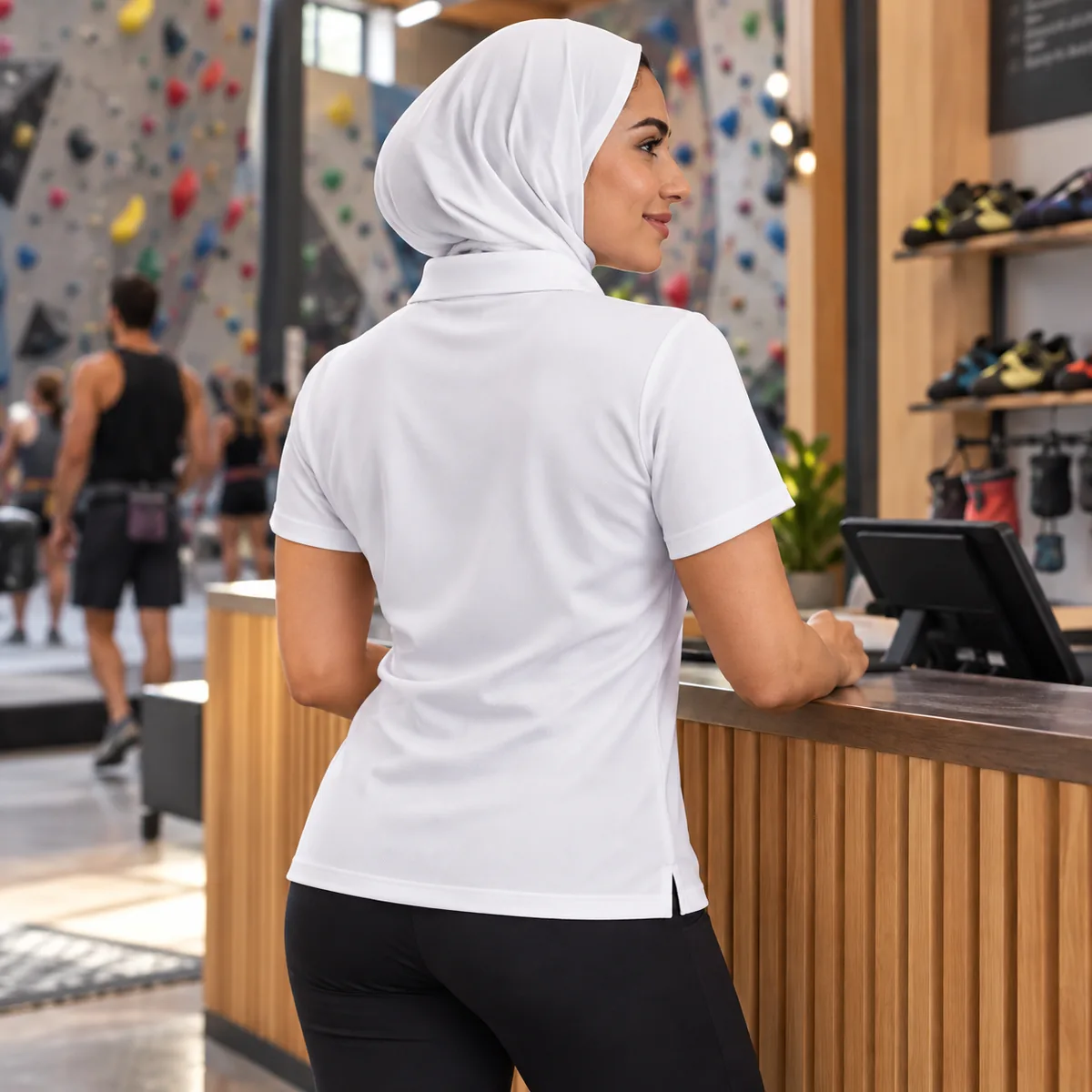 Woman wearing a white Sport-Tek micropique polo at an indoor climbing gym, shown from the back.