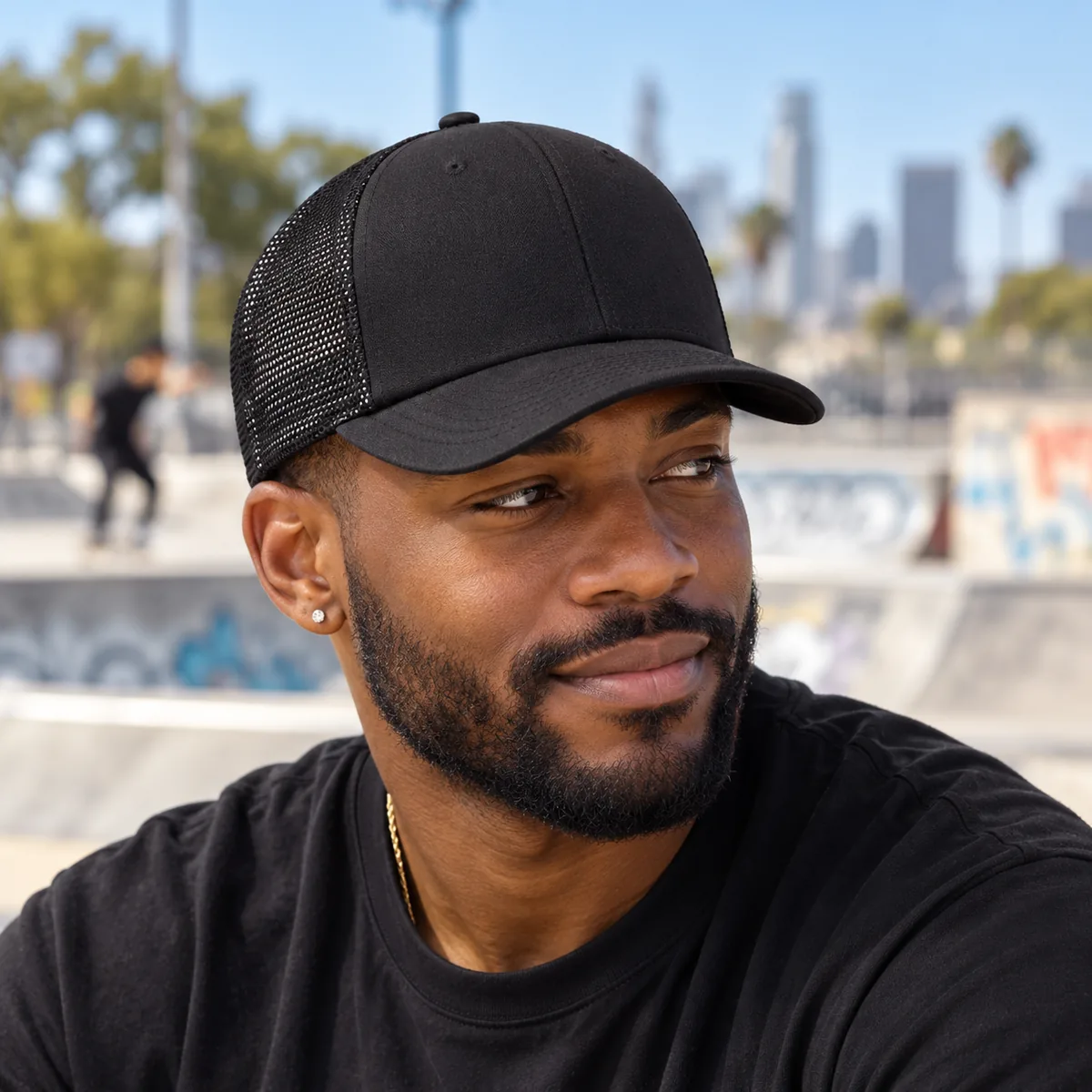 Man wearing a black blank Yupoong retro trucker cap at a city skatepark.