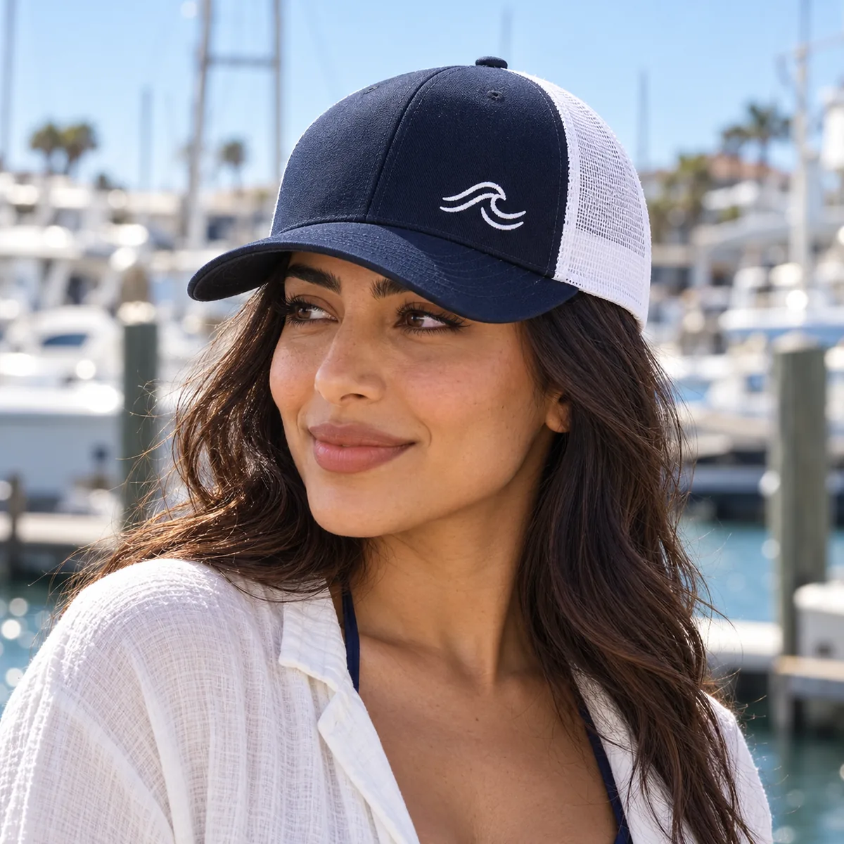 Woman wearing a navy and white trucker cap with fictional Good Current sample embroidery at a marina.