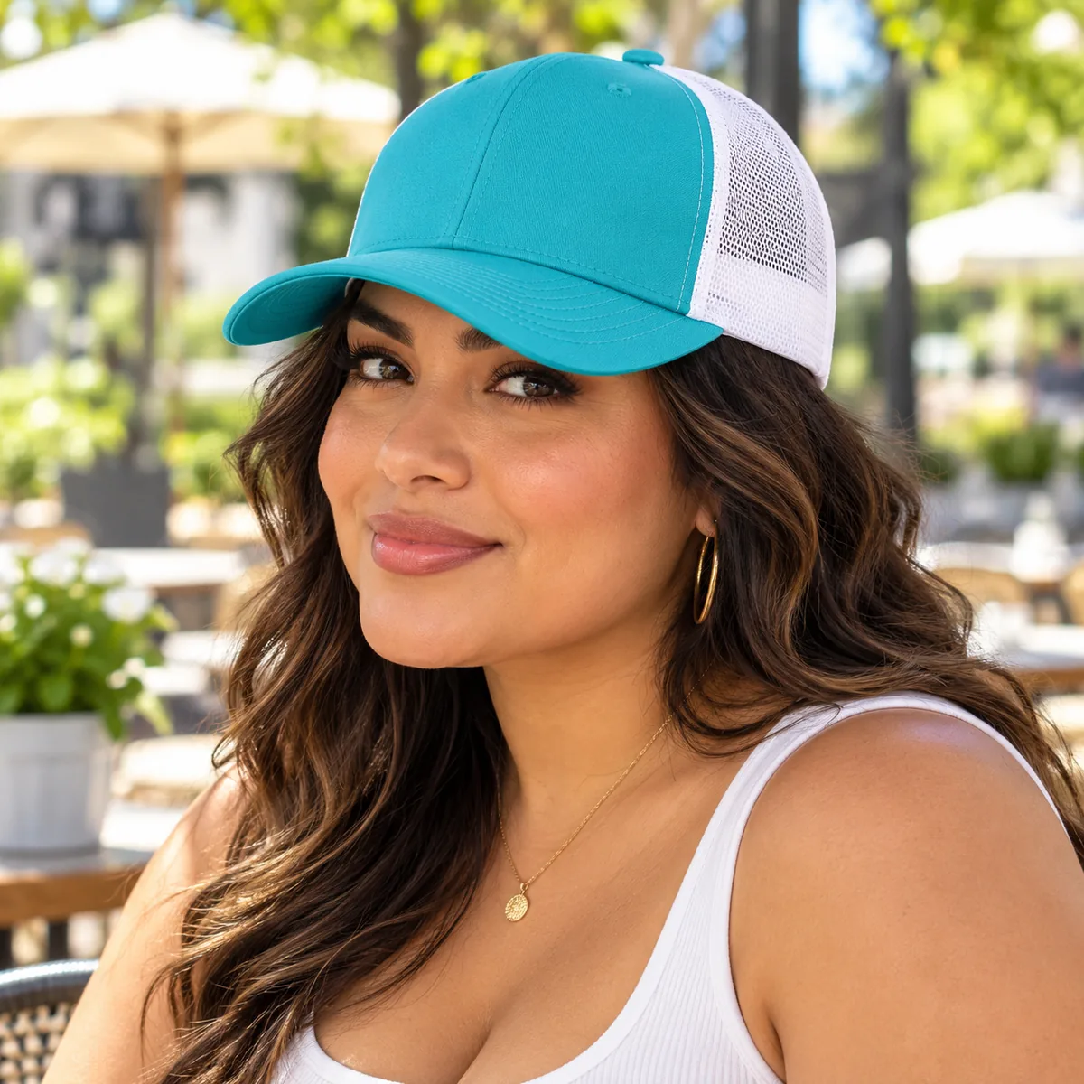 Woman wearing a turquoise and white Yupoong trucker cap at an outdoor cafe; blank front.